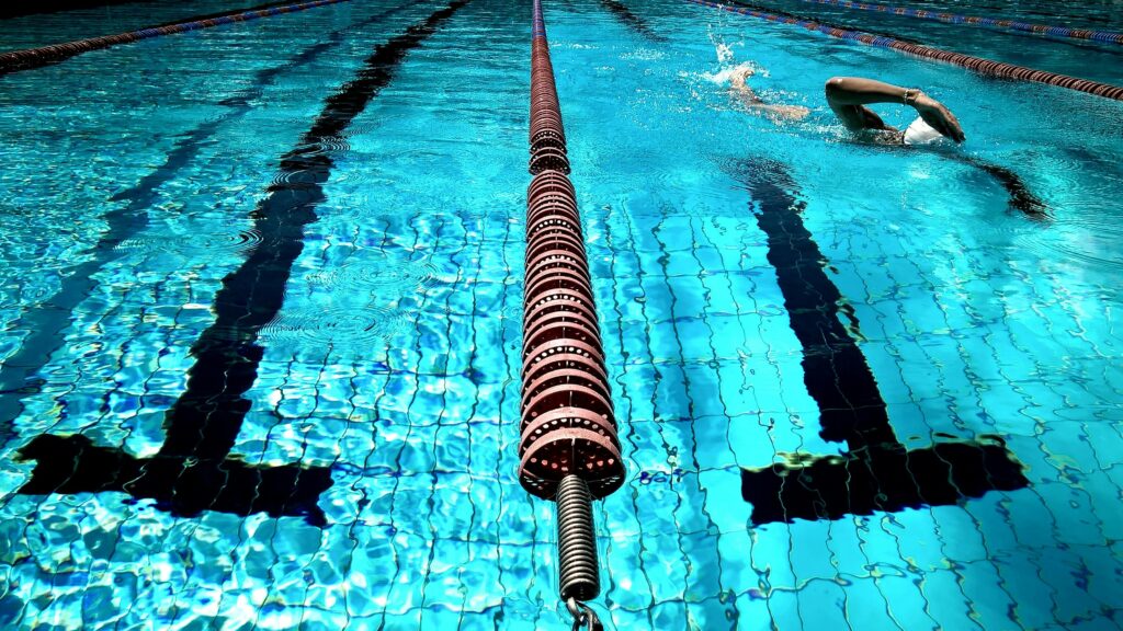 A person swimming in a clear blue outdoor pool with lane dividers.
